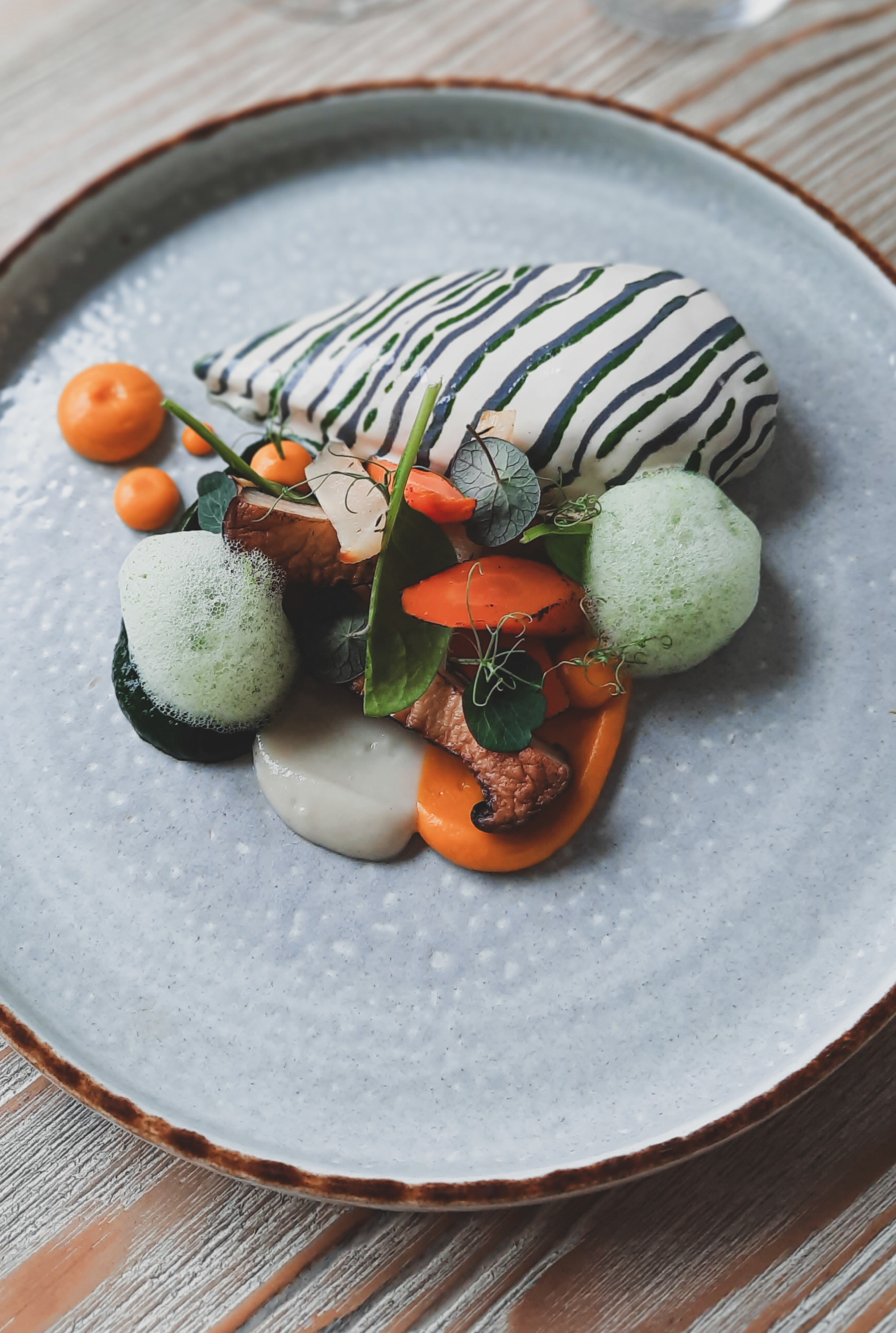 Assiette gastronomique dressée avec viande, carottes glacées et écume d'herbes