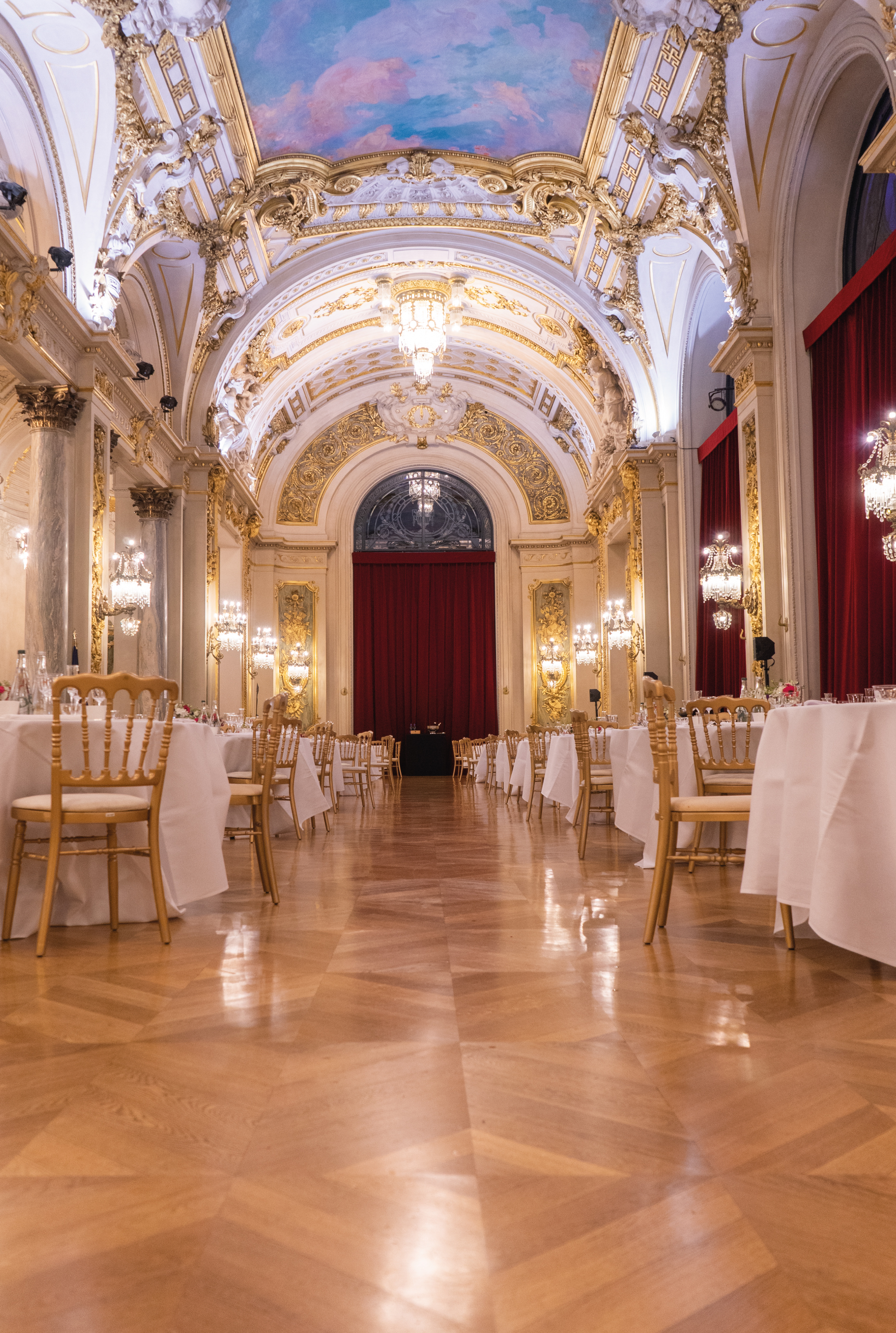 Salle de réception dorée aux lustres de cristal, tables rondes dressées pour un banquet