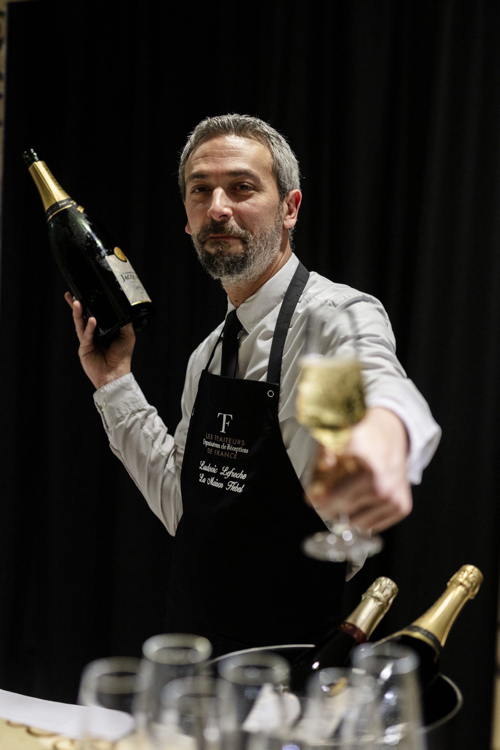 Maître d'hôtel en tablier Les Traiteurs de France servant une coupe de champagne lors d'une réception