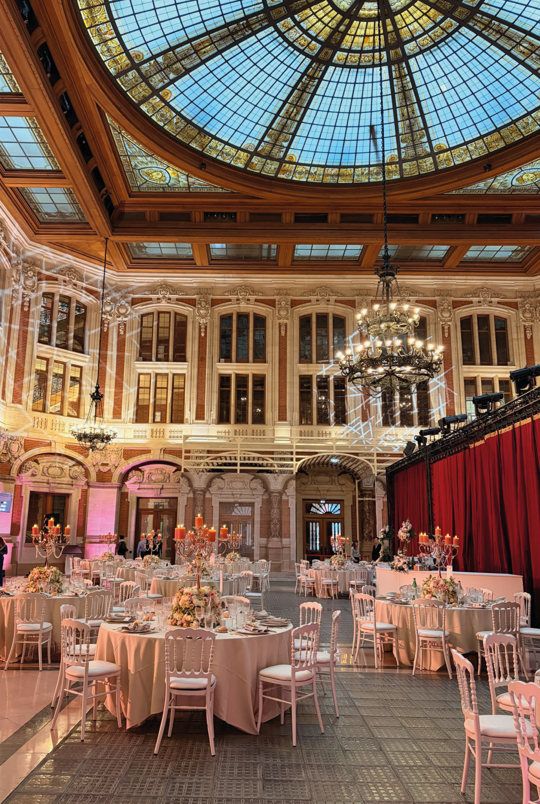 Dîner de gala sous une coupole de vitraux, tables rondes et chandeliers allumés