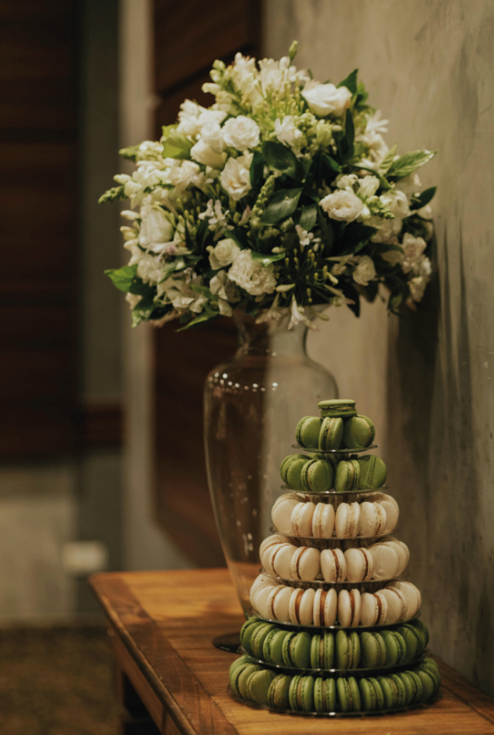 Pyramide de macarons verts et ivoire présentée près d'un bouquet de fleurs blanches
