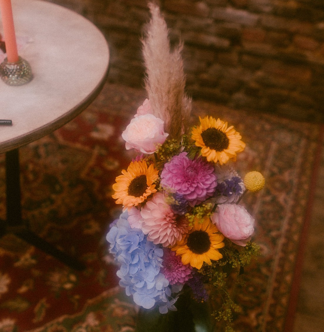 Bouquet de tournesols, dahlias, hortensia bleu, roses et herbe de la pampa posé sur un tapis oriental lors d’un mariage