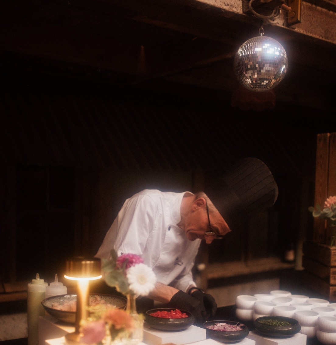 Chef Butterfly Traiteur dressant un buffet de garnitures avec poivrons, oignons rouges et herbes sous une boule à facettes