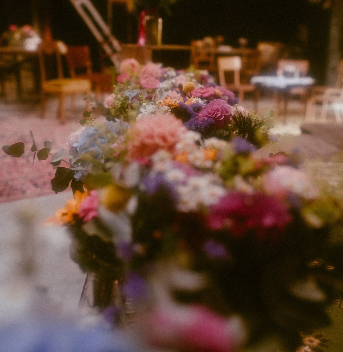 Compositions florales colorées de dahlias, hortensias et marguerites alignées sur une table de réception de mariage