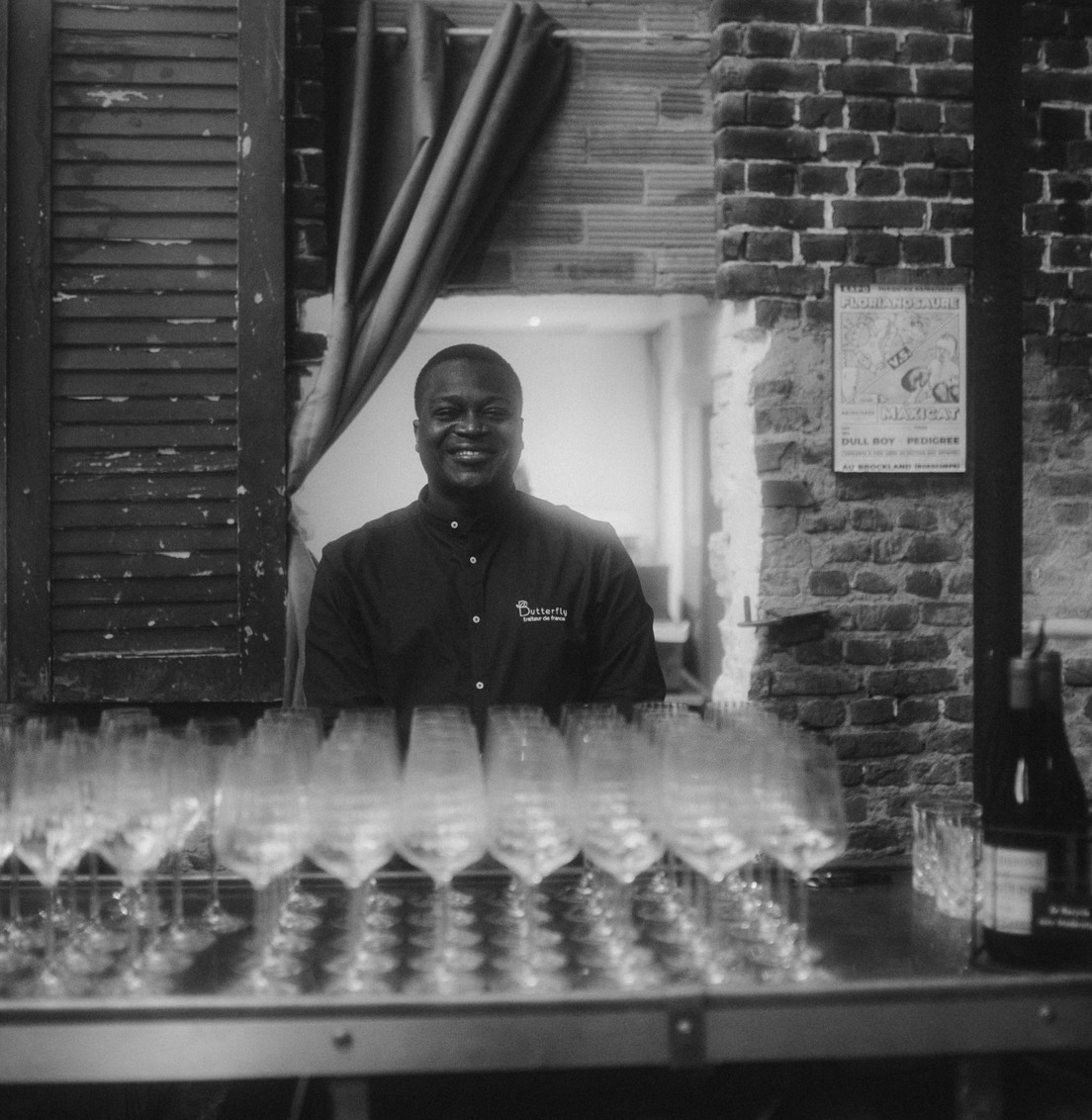 Serveur Butterfly Traiteur souriant derrière un bar garni de verres à vin dans une salle de réception en briques à Lille